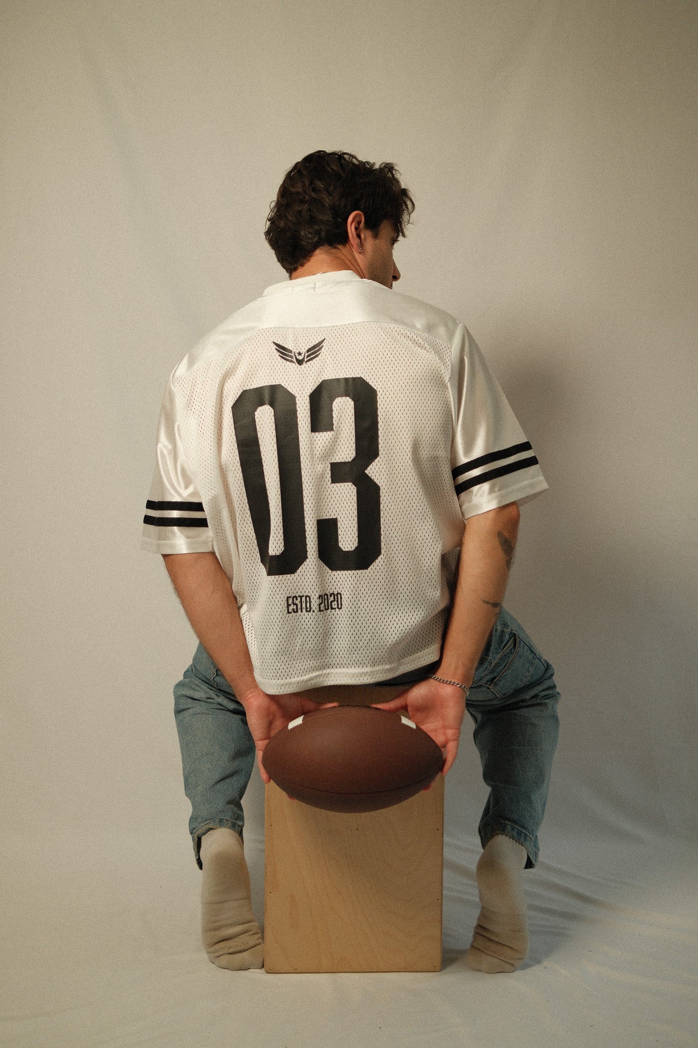 Person wearing a sports jersey with number 03, holding a football on a white background
